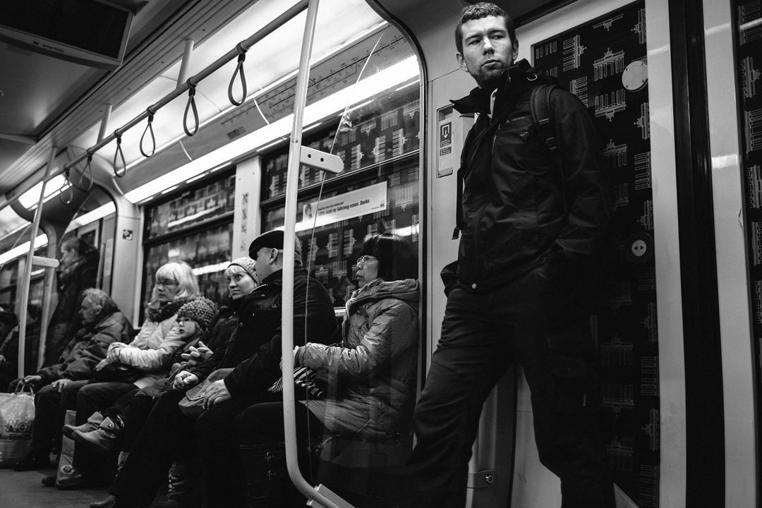 a group of people sitting on the subway, a man stands by the door