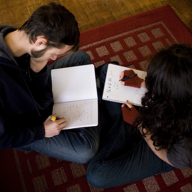 man and woman sitting on floor writing in lined notebooks