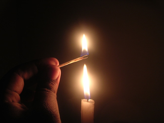 fingers holding a lit match directly above a lit candle